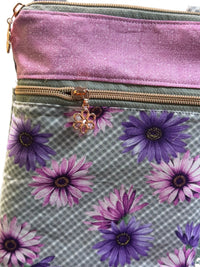 A close-up of a fabric pouch or bag with a two-tone design: a solid light purple top section and a gray-and-white gingham lower section with purple and pink daisy floral print. A rose gold zipper with a flower-shaped zipper pull is visible.