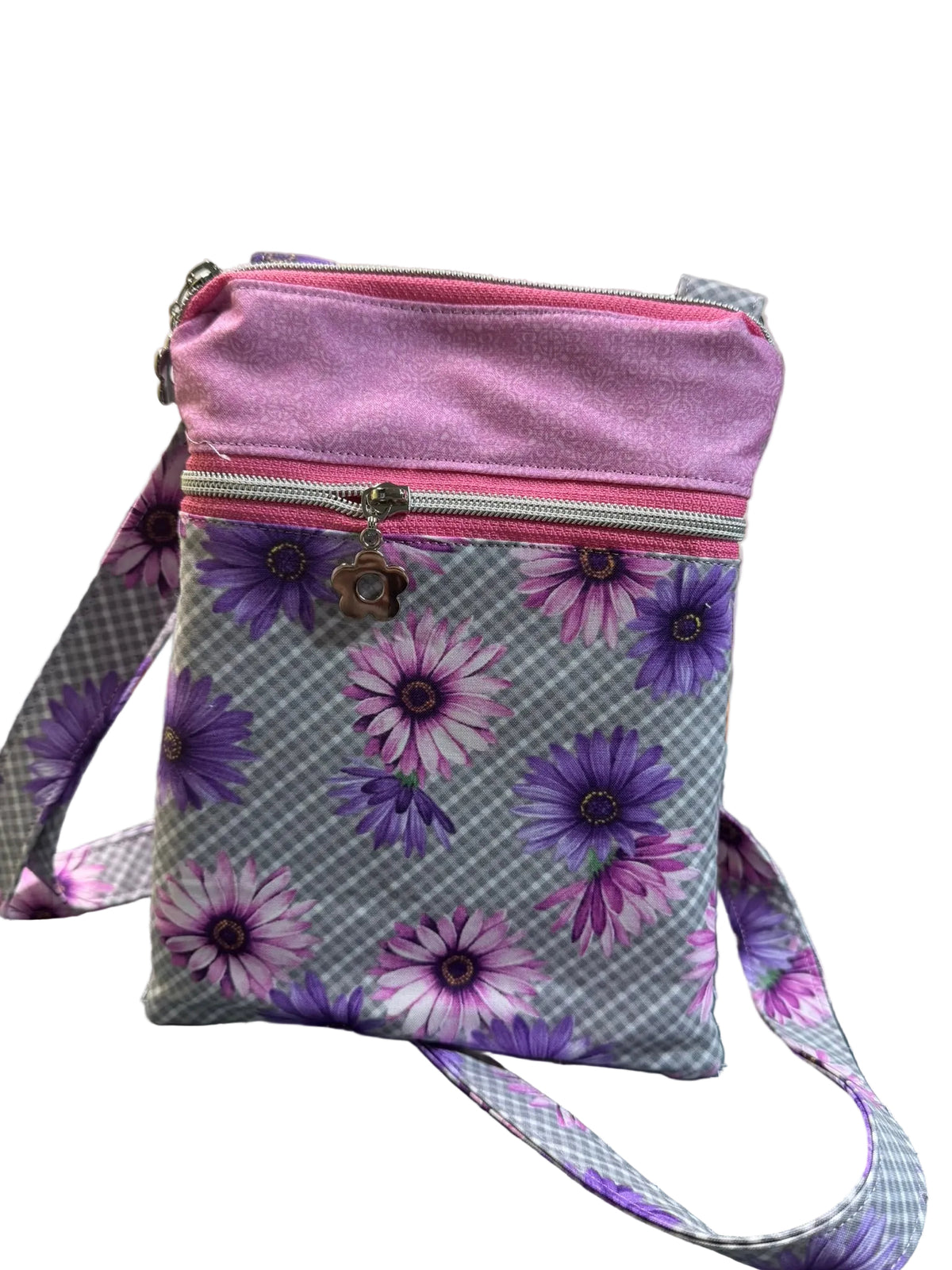 A small crossbody bag with a lavender glittery top, a gray gingham body with purple and pink daisy floral print, and a matching patterned strap,