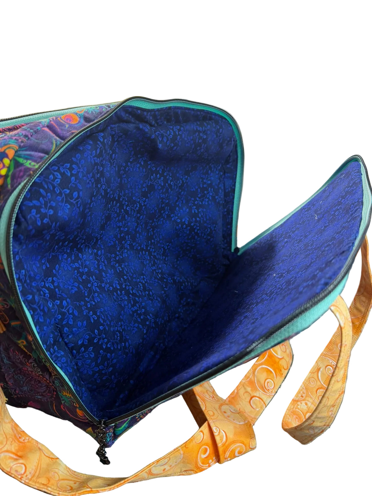 An open fabric tote bag with a dark blue patterned interior lining and teal trim, with orange patterned straps in front.