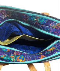 An open fabric bag with a colorful paisley pattern on the exterior and a dark blue lining with a gold inner pocket. 