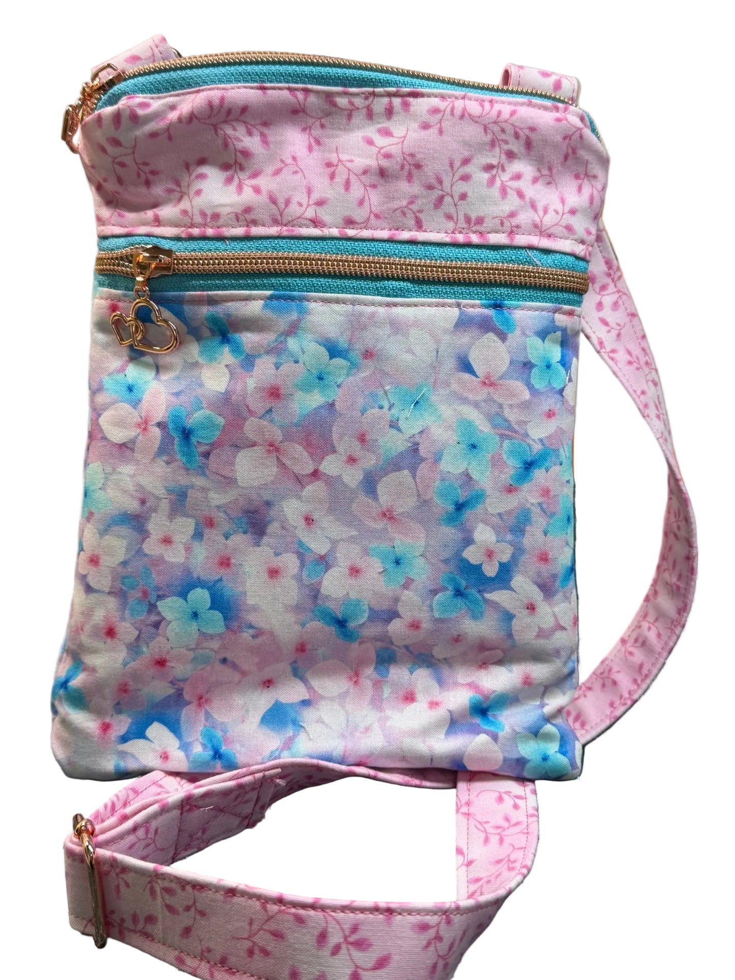 A small fabric crossbody bag with a pink floral print, turquoise zipper, and matching floral strap