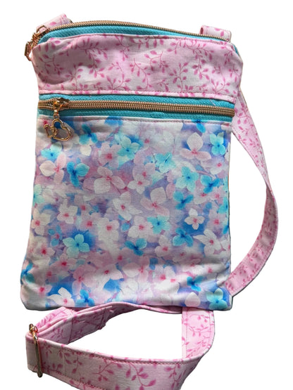 A small fabric crossbody bag with a pink floral print, turquoise zipper, and matching floral strap