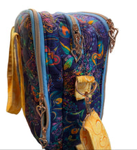A quilted fabric crossbody bag with a vibrant paisley pattern in purple, blue, orange, and green, featuring gold-tone hardware and a matching patterned strap.