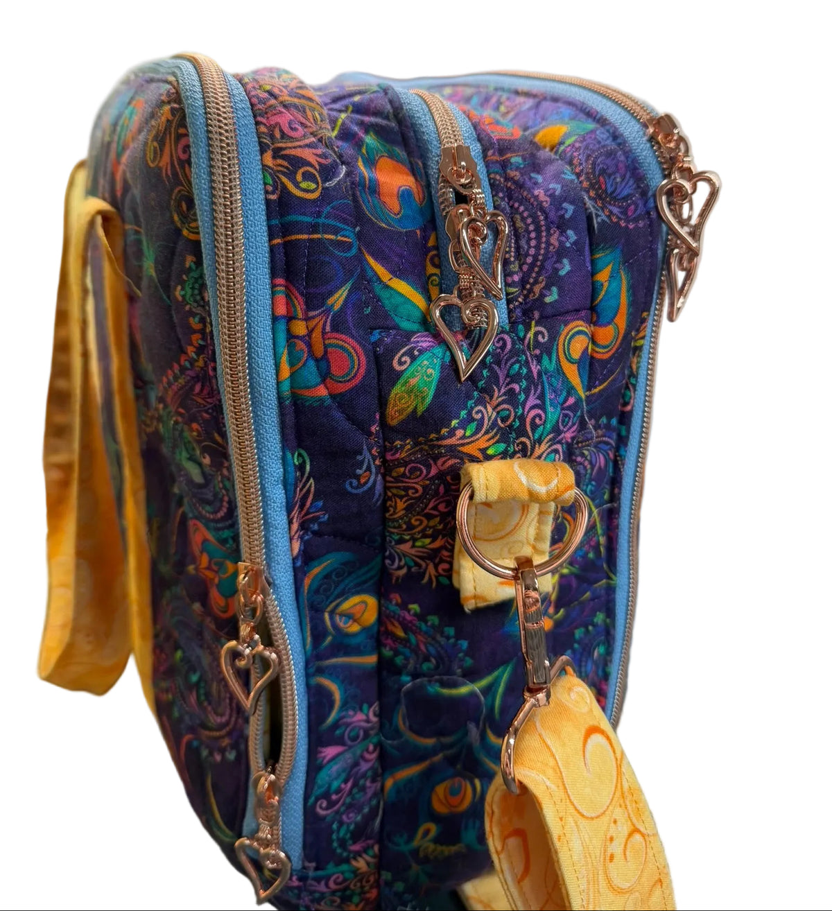 A quilted fabric crossbody bag with a vibrant paisley pattern in purple, blue, orange, and green, featuring gold-tone hardware and a matching patterned strap.