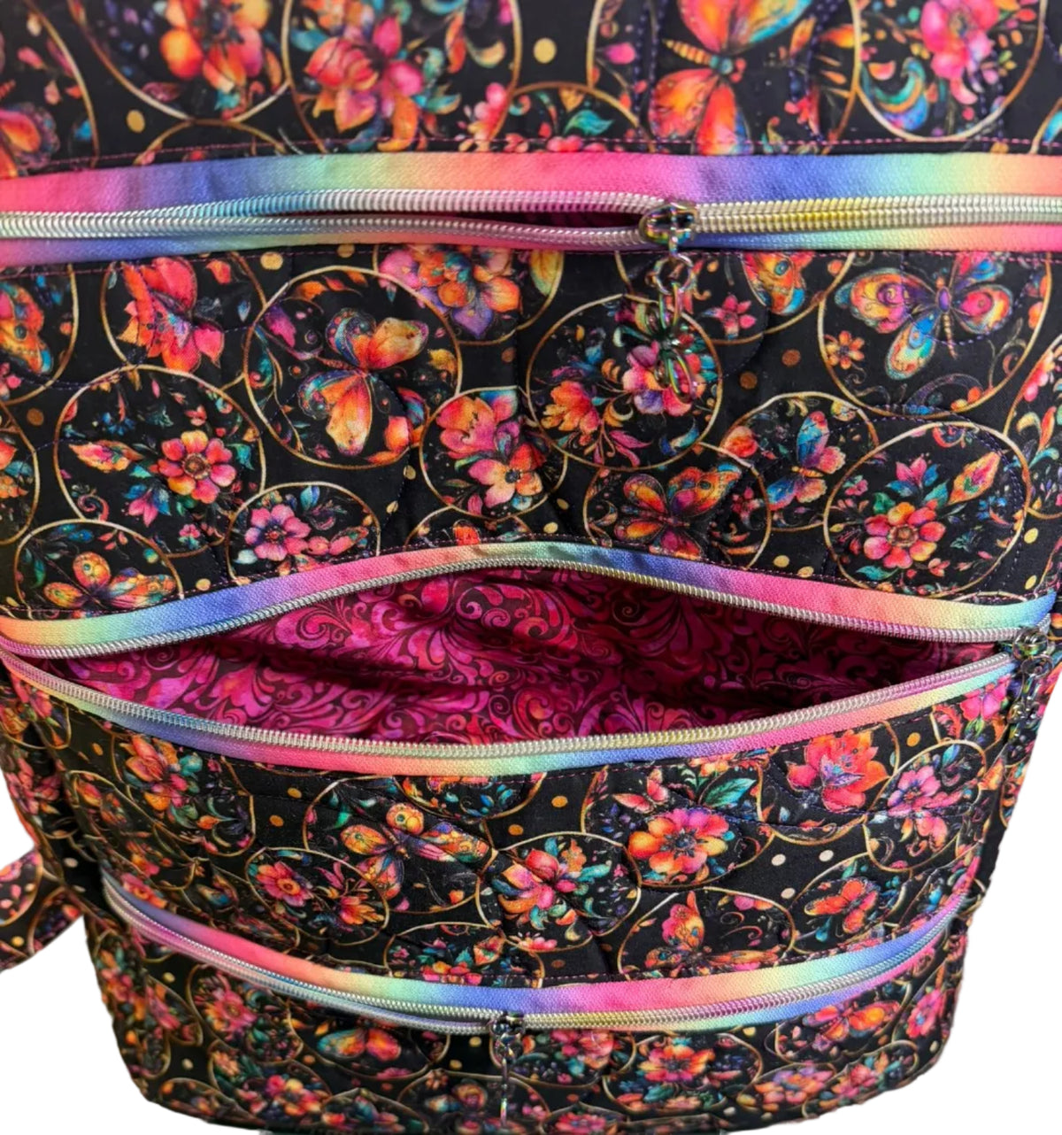 A close-up of a fabric zippered pouch or organizer with a black background, colorful butterfly and floral print, and iridescent rainbow zipper trim.