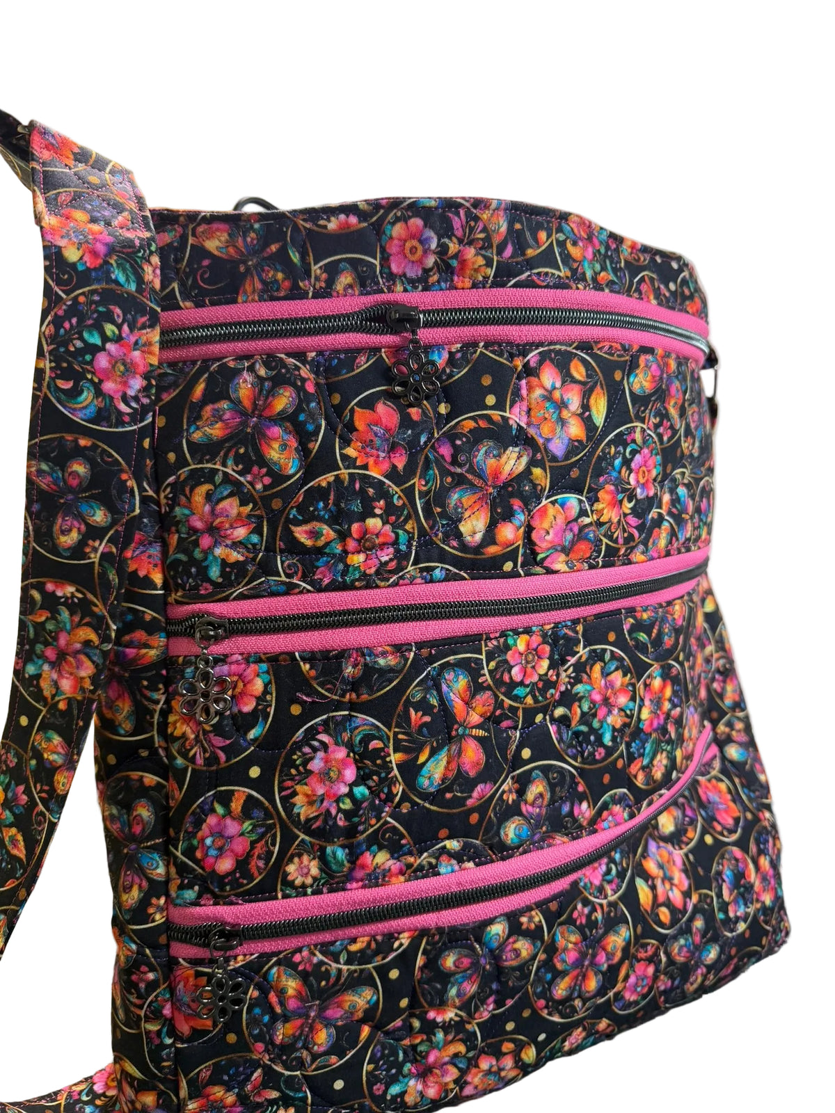 A fabric tote bag with a black background and a colorful butterfly and floral pattern, featuring three horizontal pink zippers.