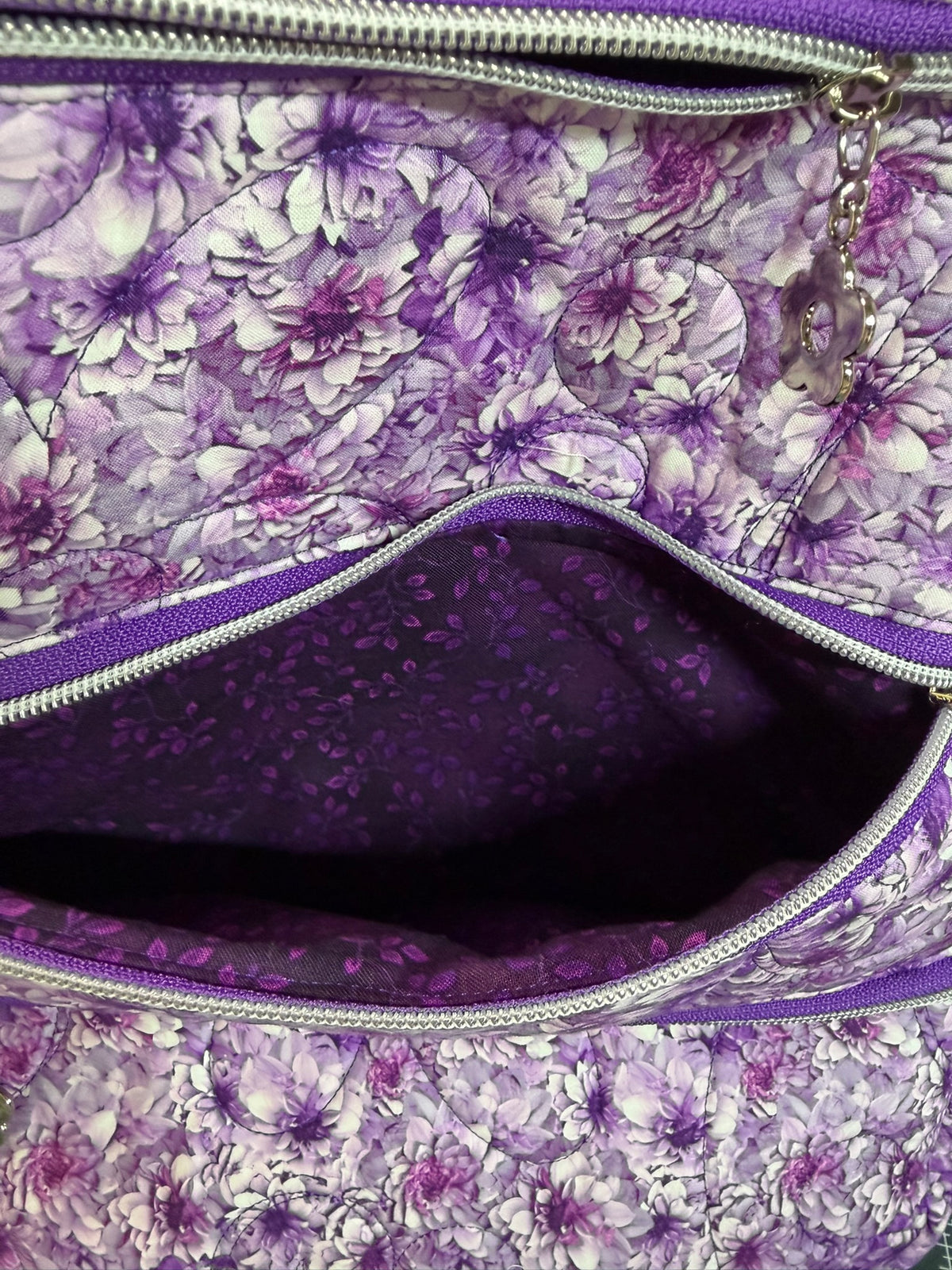 Close-up of a purple and white floral patterned bag with silver zippers, showing the interior lining and a zipper pull.