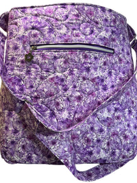 A quilted fabric bag with a purple and white floral pattern, featuring a front zippered pocket and a curved flap.