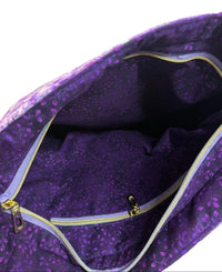 Close-up of the inside of a purple patterned fabric bag with a zippered pocket, showing the interior lining and gold-toned zipper.