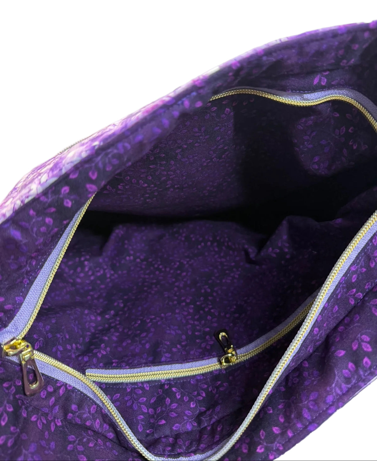Close-up of the inside of a purple patterned fabric bag with a zippered pocket, showing the interior lining and gold-toned zipper.