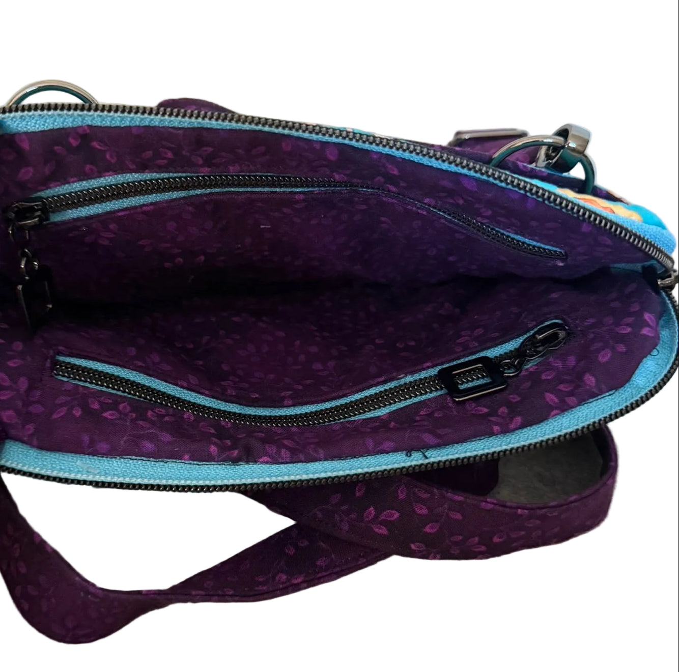 A purple patterned crossbody bag with a light blue zipper trim.