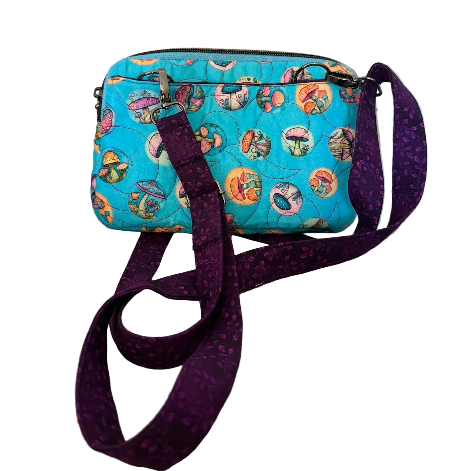 A small crossbody bag with a turquoise blue background and a colorful circular pattern, featuring a wide purple patterned strap.