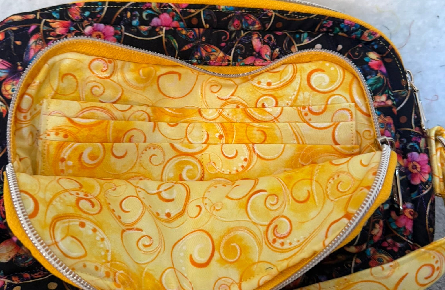 A close-up of a small zippered bag with yellow and orange swirl-patterned interior and a black floral exterior. 