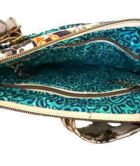 A close-up of a hand holding open a patterned clutch showing a teal and blue swirled fabric exterior and interior lining with gold-toned zippers.