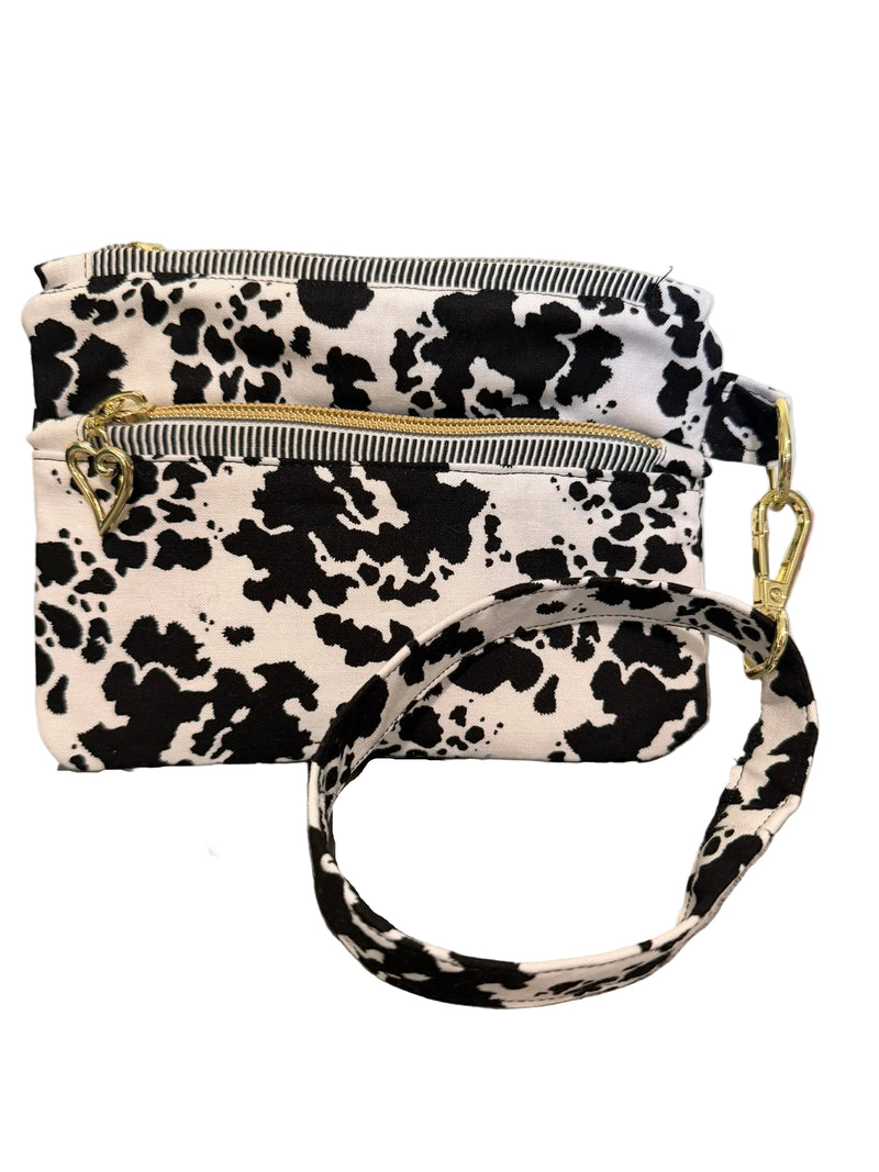 A small crossbody bag with a black and white cow print pattern, featuring gold-tone hardware and a matching wrist strap, 