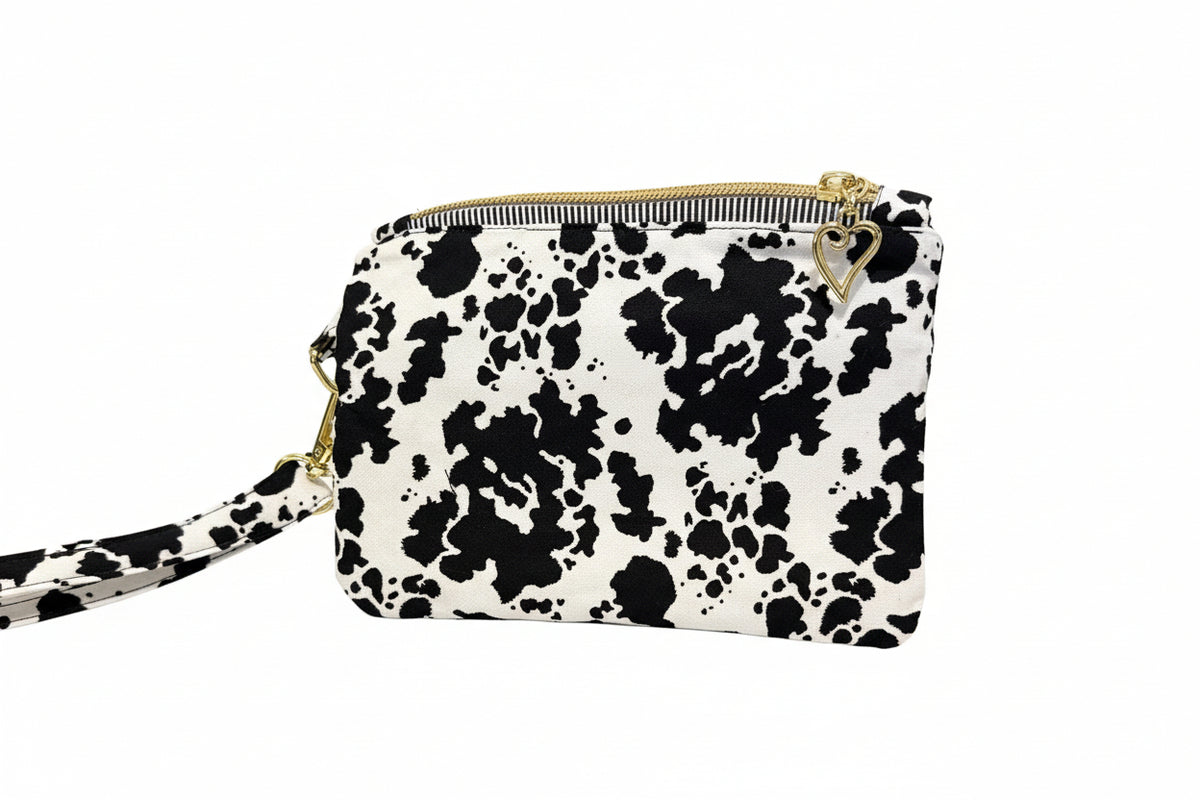 A small black and white cow print pouch bag with gold zipper and hardware, 