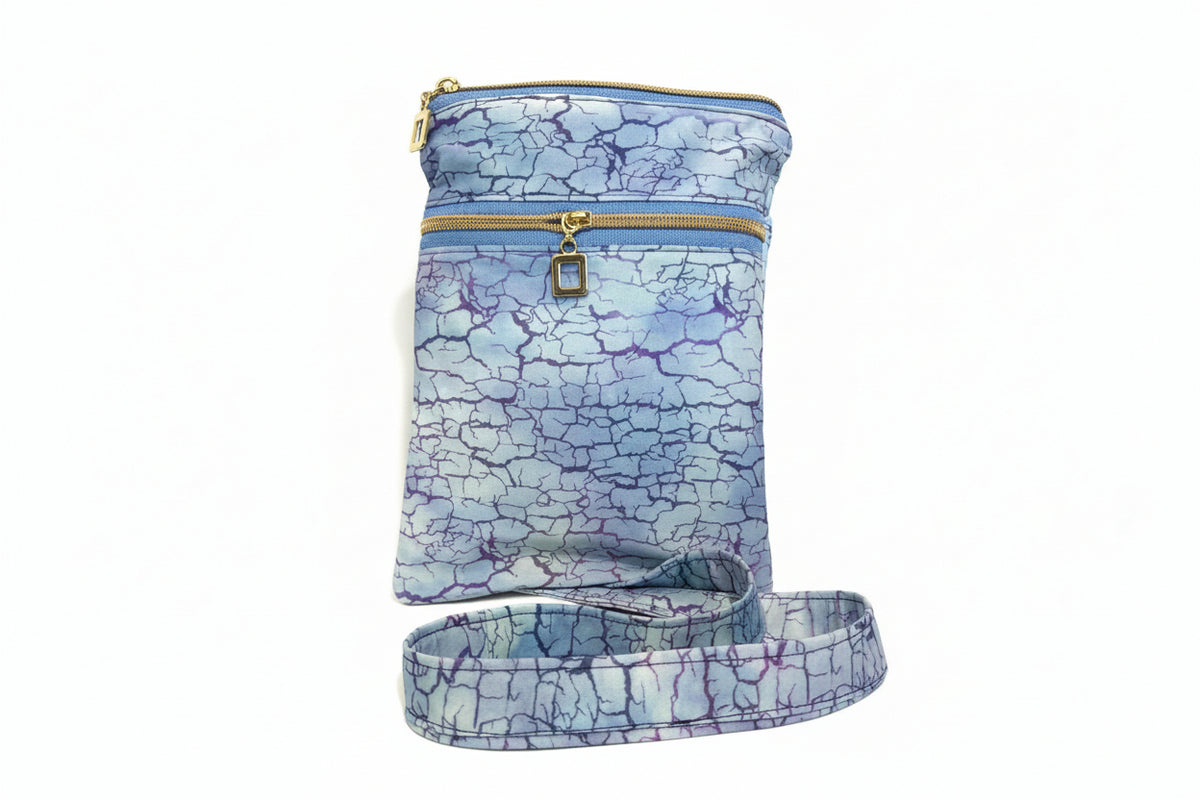 A fabric crossbody bag with a blue and purple crackle pattern, featuring gold zippers and a matching adjustable shoulder strap,