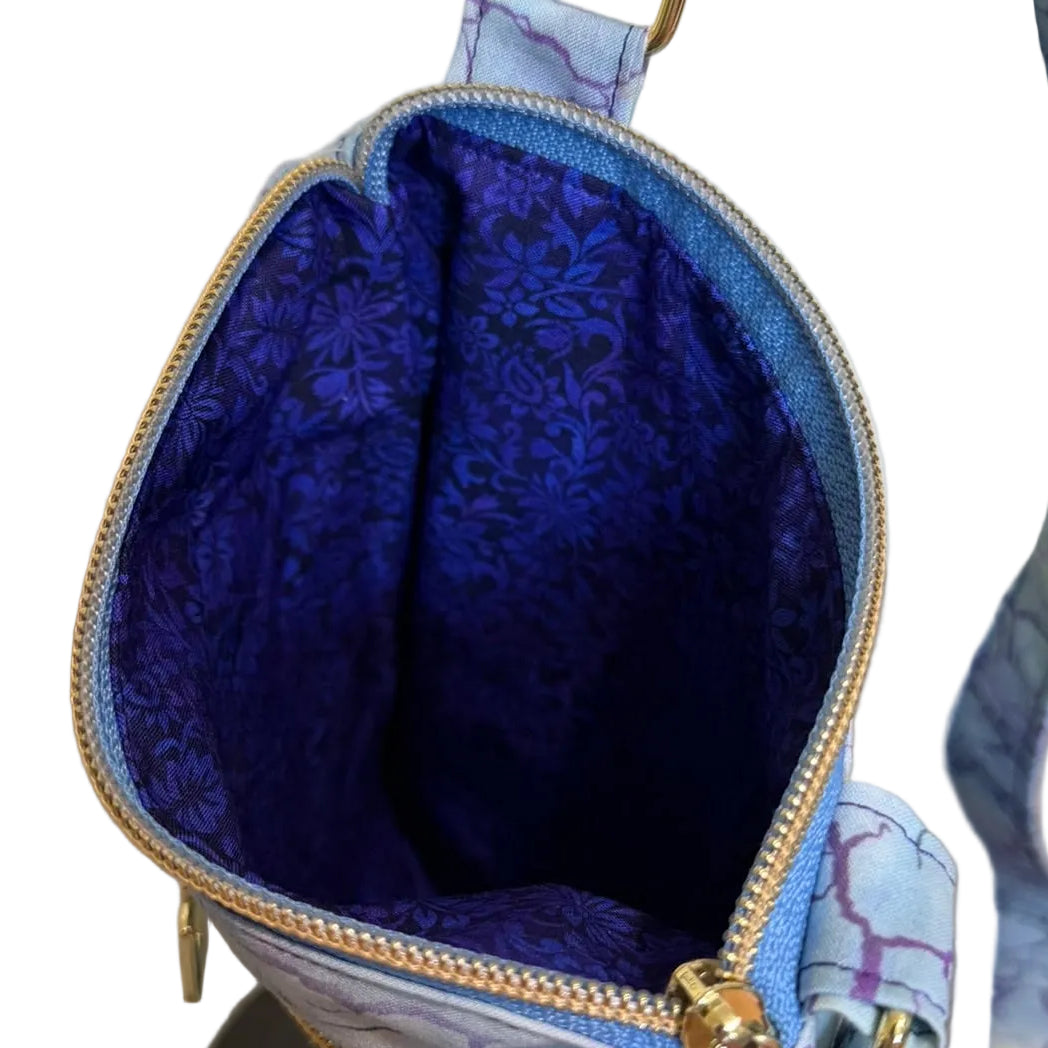 A close-up of a small crossbody bag with a light blue and purple marble-patterned exterior, a bright royal blue patterned lining.