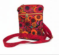 A small crossbody bag with a vibrant sunflower print on a red background, featuring a matching red fabric strap and a gold-tone zipper pull