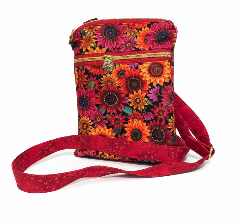 A small crossbody bag with a vibrant sunflower print on a red background, featuring a matching red fabric strap and a gold-tone zipper pull