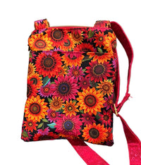 A small fabric crossbody bag with a vibrant sunflower print in red, orange, pink, and yellow on a black background,  The bag has a red strap.