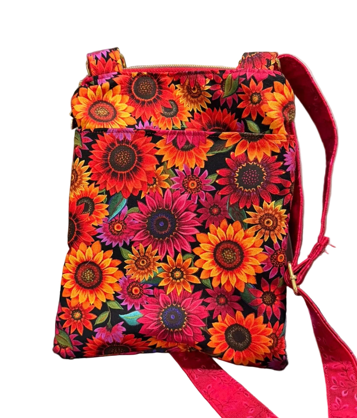 A small fabric crossbody bag with a vibrant sunflower print in red, orange, pink, and yellow on a black background,  The bag has a red strap.